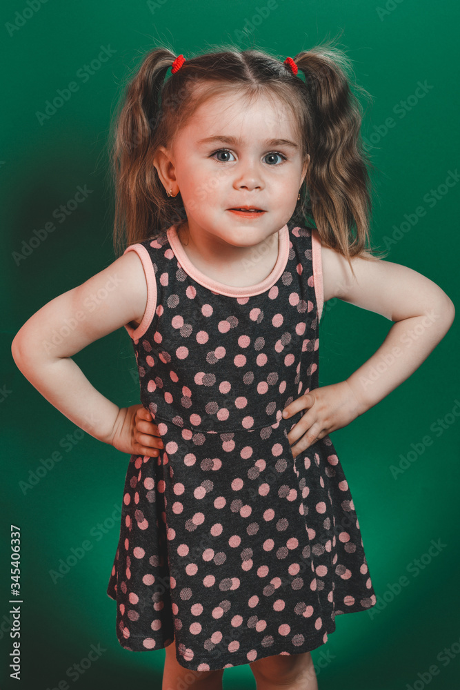 Little girl of three years with tails in dress posing in studio on green background Little girl of three years with tails in dress posing in studio on green background