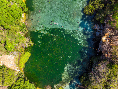 Aerial of Tourists swimming and enjoying the summer on beautiful and crystalline green water at River Pratinha, Iraquara, Chapada Diamantina, Bahia, Brazil. Drone slowly moving up.