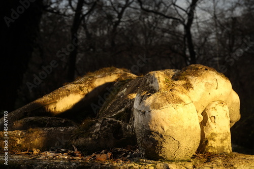 Decaying mossy sculpture in a garden dramatically lit by golden hour. Figure man lying on his back  photo