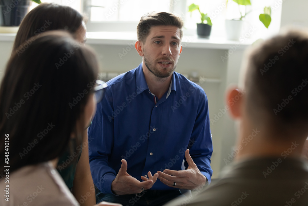 Obraz premium Confident serious male coach mentor talking holding briefing for team employees in office, sharing business strategy. Businessman sitting at company meeting with diverse colleagues.