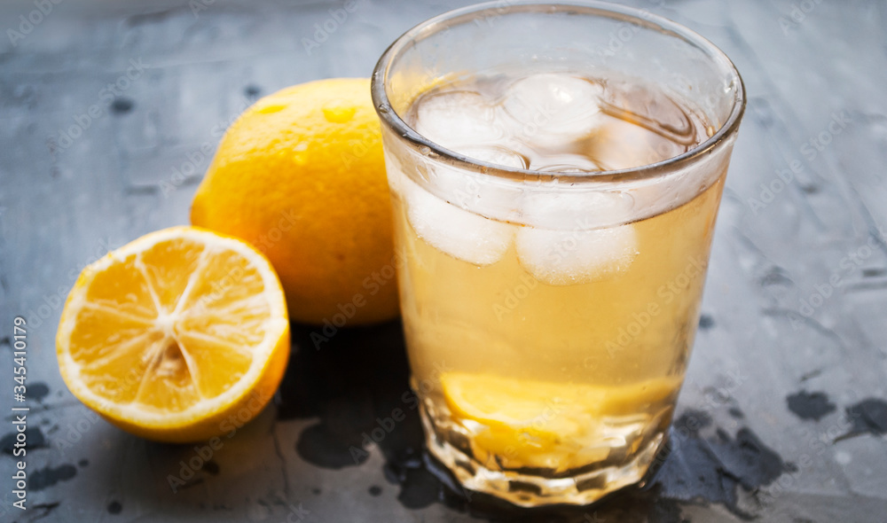 Homemade lemonade with ice in a glass. Glass, lemons and drops on a gray background. Homemade lemonade with ice in a glass. Glass, lemons and drops on a gray background.