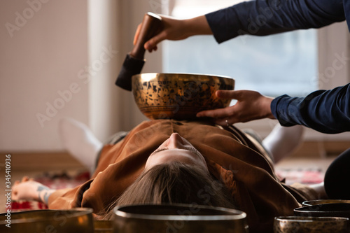 Woman making relaxing massage, meditation, sound therapy with tibetian singing bowls. Stress relief. Selective focus on female face. Bottom view.  photo