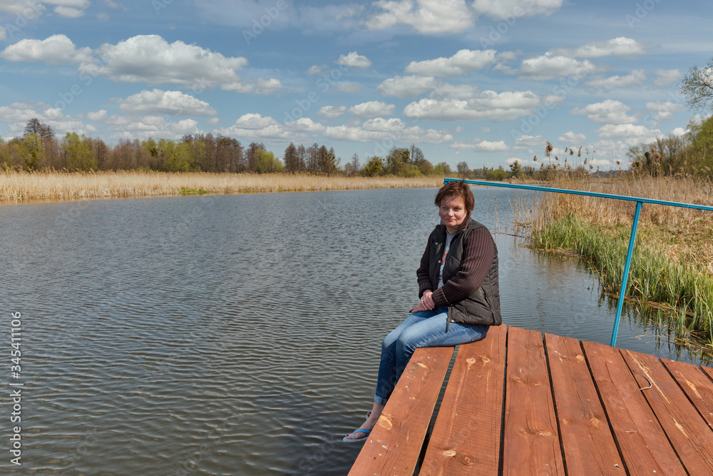 Woman facing at river while sitting on wooden pavement