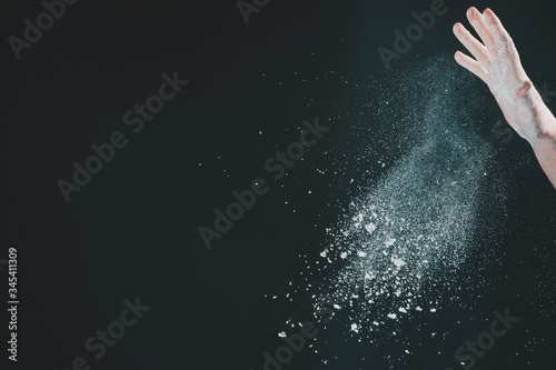 Hand of european woman chef in kitchen pouring flour on black background