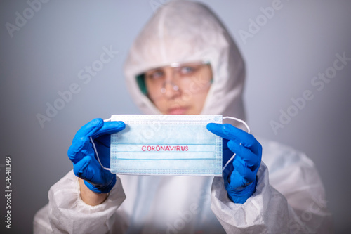 COVID-19. 2019 Novel Coronavirus  2019-nCoV  concept. Young girl doctor in a white protective anti-plague coat holding a medical mask with the inscription Coronavirus