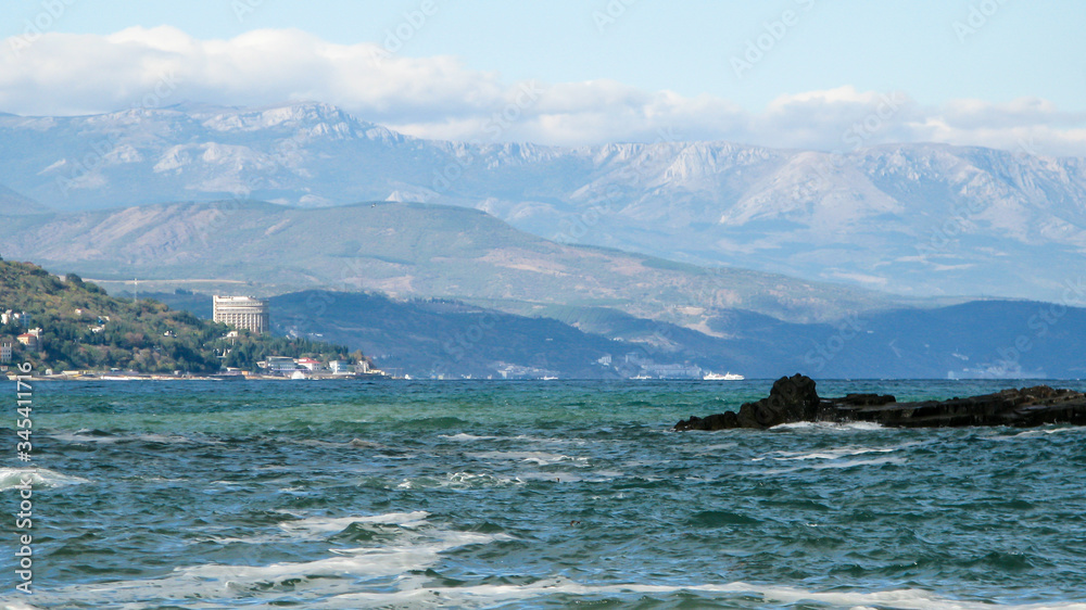 panoramic view of the sea with mountains in the background, blue sky and clouds