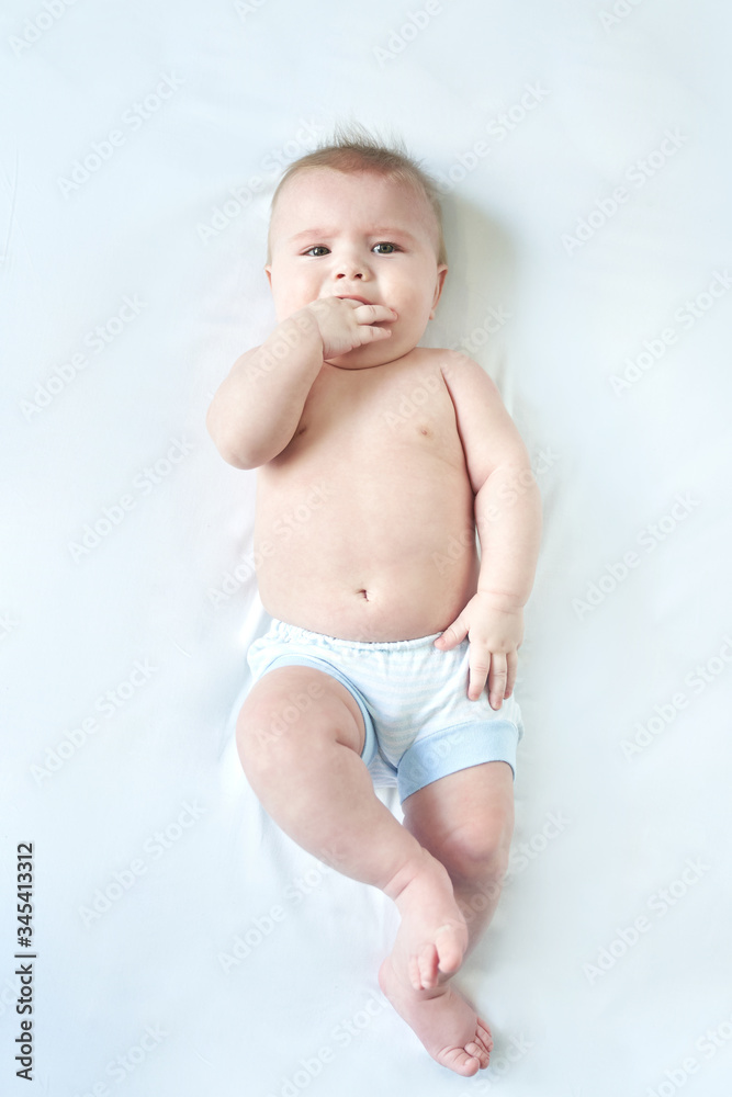 a wonderful baby lies on a white sheet for six months and wants to cry . the hand in his mouth. teething a wonderful baby lies on a white sheet for six months and wants to cry . the hand in his mouth. teething