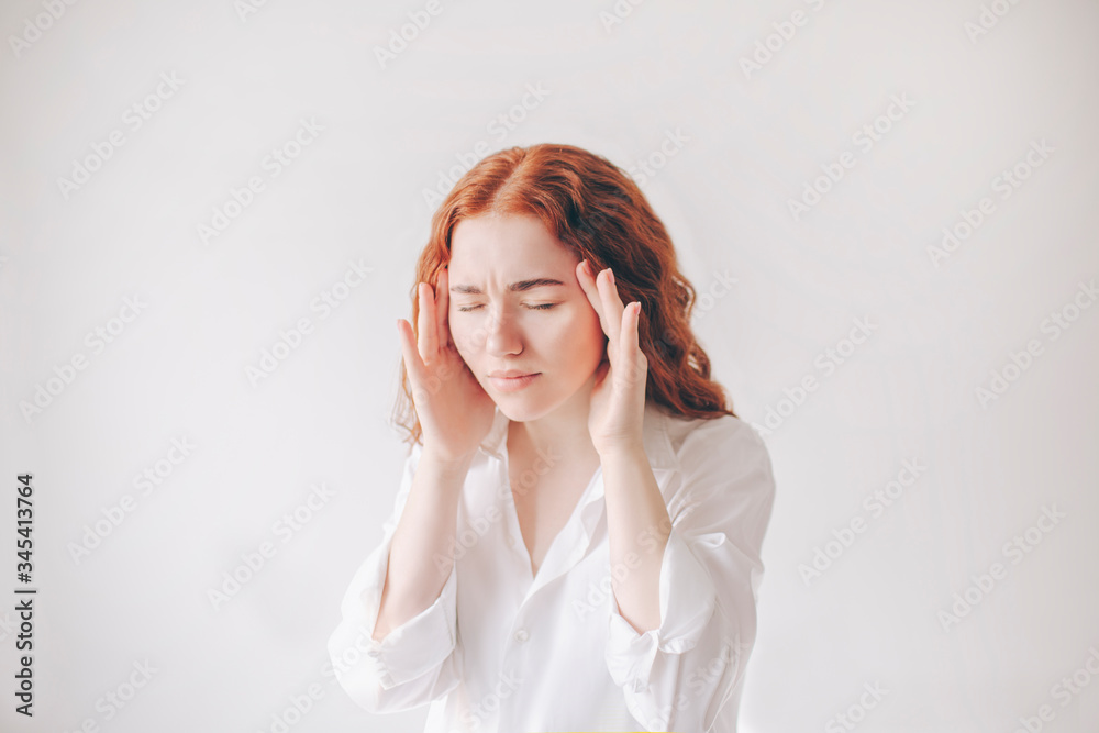 Young, red-haired woman isolated on a white background in a white T-shirt has a headache and migraine Young, red-haired woman isolated on a white background in a white T-shirt has a headache and migraine