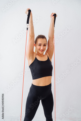 Concept of sports without a gym and sports simulators. Muscular girl fitness trainer showing how exercise at home with a tubular red expander. She ties it to the door and holding it by feets