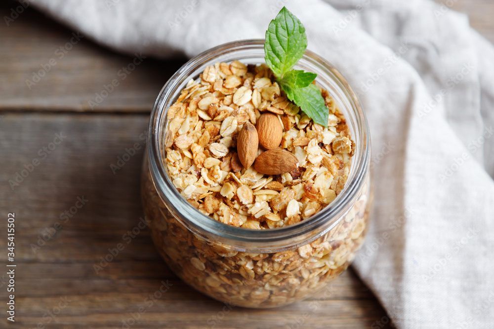Homemade oatmeal granola in an open glass jar, decorated with nuts and a leaf of mint on a wooden table. Healthy breakfast, fitness food, weight loss. Place for text Homemade oatmeal granola in an open glass jar, decorated with nuts and a leaf of mint on a wooden table. Healthy breakfast, fitness food, weight loss. Place for text