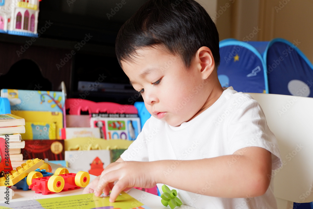 An Asian boy is playing a toy on a white table. An Asian boy is playing a toy on a white table.