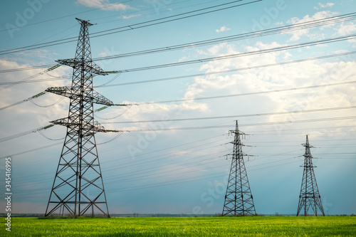 High voltage lines and power pylons in a flat and green agricultural landscape on a sunny day with clouds in the blue sky. Cloudy and rainy. Wheat is growing