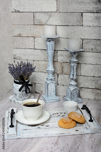 Composition of a cup of coffee and cookies on a wooden tray, dry lavender in a white vase and decorative candlesticks.