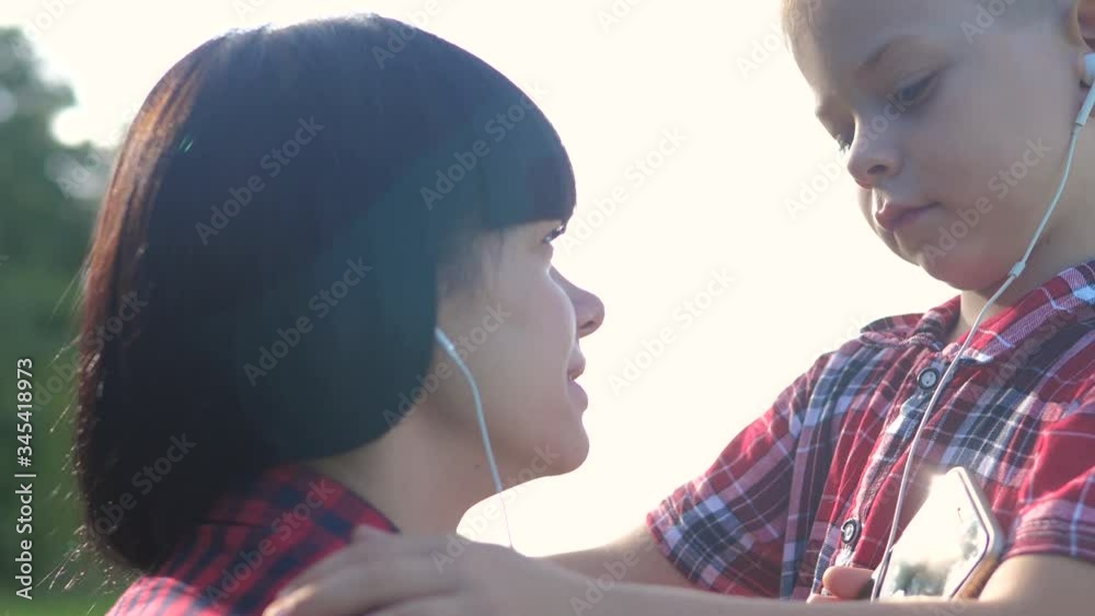 ehappy family funny nature slow motion video teamwork outdoors. Mom and son listen to music on smartphone in the same headphones for two . happy family mother woman and little lifestyl son boy spend ehappy family funny nature slow motion video teamwork outdoors. Mom and son listen to music on smartphone in the same headphones for two . happy family mother woman and little lifestyl son boy spend
