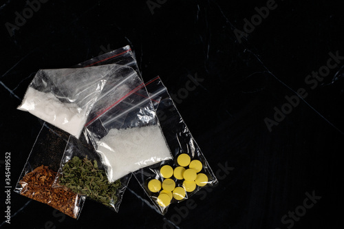 lethal concept: tobacco, weed, MDMA tablets, amphetamine crystals, heroin in plastic bags, on a dark background. Enhanced contrast, partial blur.