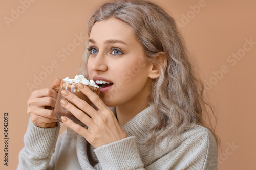 Beautiful young woman with cup of hot chocolate on color background