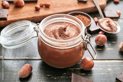 Jar with tasty chocolate paste and hazelnuts on table