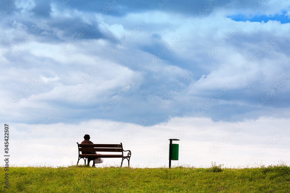 Line horizon and earth on a background of beautiful blue clouds. One woman sits on a bench and looks at the sea. Horizontal frame. Color photography. Line horizon and earth on a background of beautiful blue clouds. One woman sits on a bench and looks at the sea. Horizontal frame. Color photography.