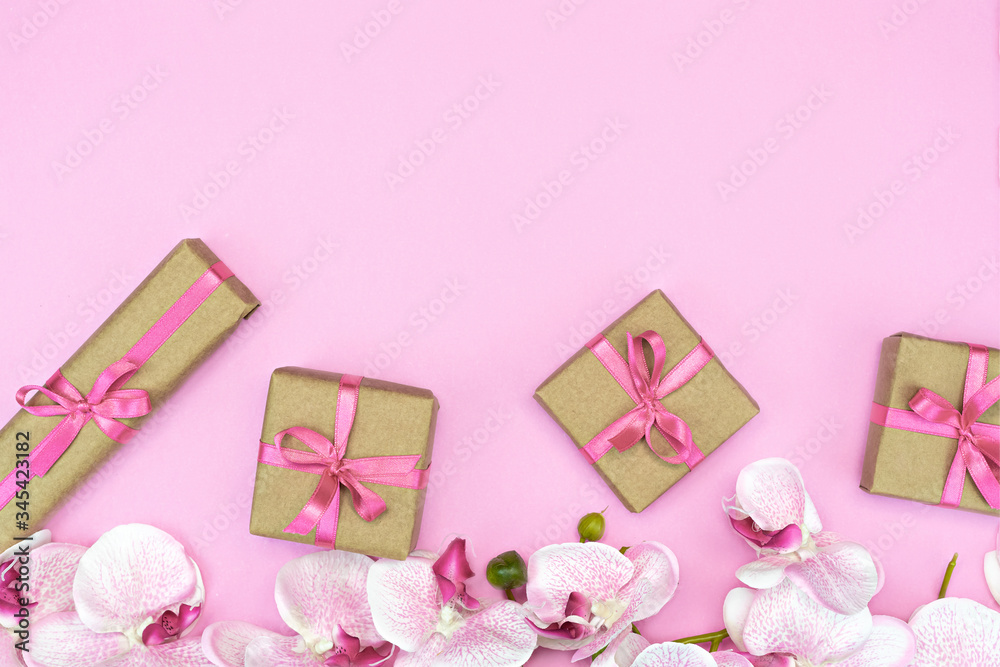 flatlay of Gift present boxes with pink ribbon, orchid flowers on pink background. Copy space