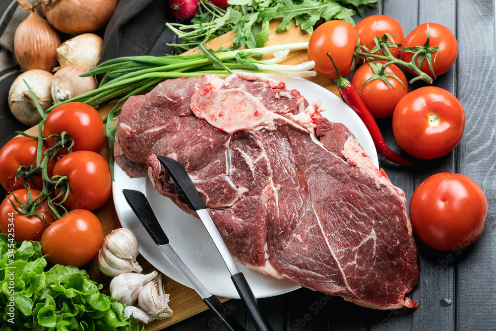 The preparation of fresh meat. Fresh beef steak on a wooden table. Meat surrounded by spices and vegetables. Fresh fruit. Red ripe tomatoes. Dietary food. The preparation of fresh meat. Fresh beef steak on a wooden table. Meat surrounded by spices and vegetables. Fresh fruit. Red ripe tomatoes. Dietary food.