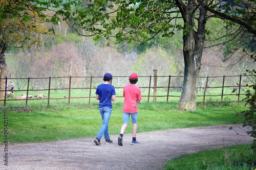 Fototapeta Naklejka Na Ścianę i Meble -  Two teenager walking in a country line with a  wrought iron park lane fence in the background