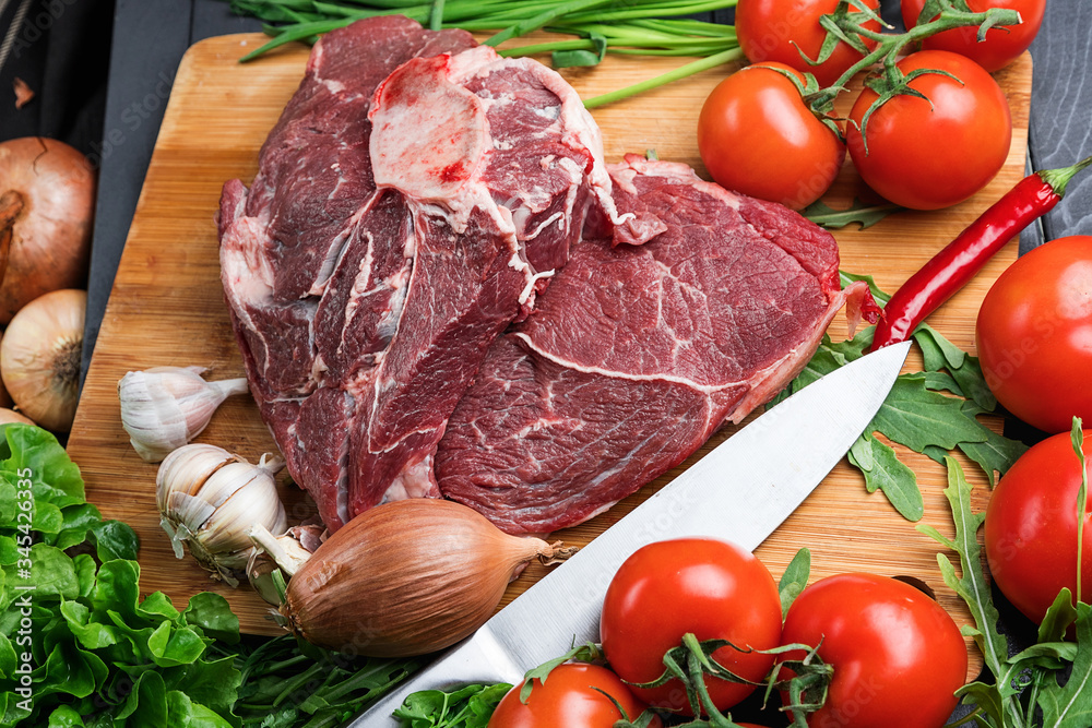 The preparation of fresh meat. Fresh beef steak on a wooden table. Meat surrounded by spices and vegetables. Fresh fruit. Red ripe tomatoes. Dietary food. The preparation of fresh meat. Fresh beef steak on a wooden table. Meat surrounded by spices and vegetables. Fresh fruit. Red ripe tomatoes. Dietary food.