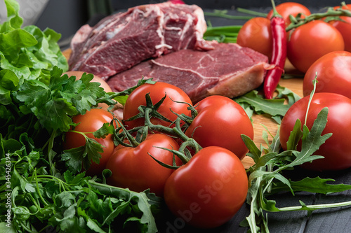 The preparation of fresh meat. Fresh beef steak on a wooden table. Meat surrounded by spices and vegetables. Fresh fruit. Red ripe tomatoes. Dietary food.