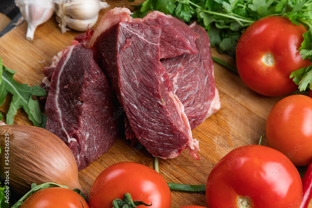The preparation of fresh meat. Fresh beef steak on a wooden table. Meat surrounded by spices and vegetables. Fresh fruit. Red ripe tomatoes. Dietary food. The preparation of fresh meat. Fresh beef steak on a wooden table. Meat surrounded by spices and vegetables. Fresh fruit. Red ripe tomatoes. Dietary food.