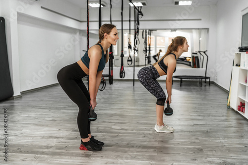 Athletic girls exercising with kettle bell while being in squat position. Muscular girls doing cross fit workout atmodern gym
