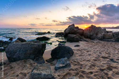 dramatic sunrise on the sea shore. waves crashing rocks on sandy beach. beautiful cloudscape above the horizon