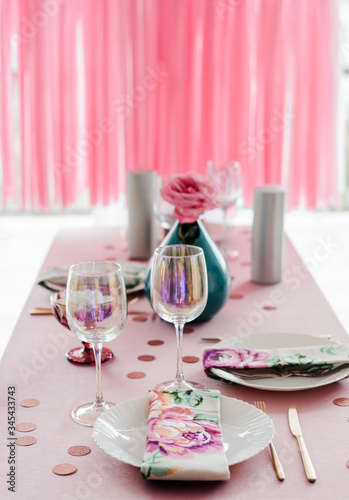 Birthday table setting in pink and colors with rose in vase. Streamers garland background. Baby shower or girl party.