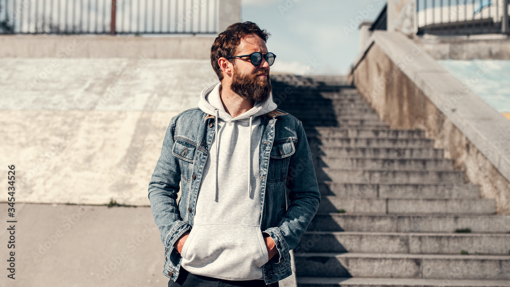 City portrait of handsome hipster guy with beard wearing gray blank hoodie or hoody with space for your logo or design. Mockup for print City portrait of handsome hipster guy with beard wearing gray blank hoodie or hoody with space for your logo or design. Mockup for print