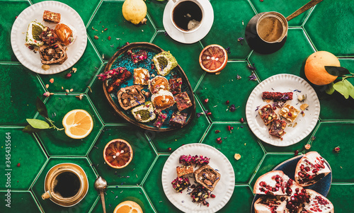 Flat-lay of variety of Turkish traditional lokum sweet delight with Turkish coffee in cups over green Moroccan tile table, top view. Middle East typical dessert food