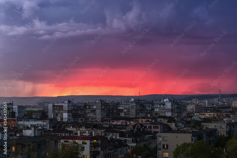 A storm is approaching the city in the late evening. Gleams of distant lightning reddened the sky above the hills outside the city. Scenic cityscape just before the storm.