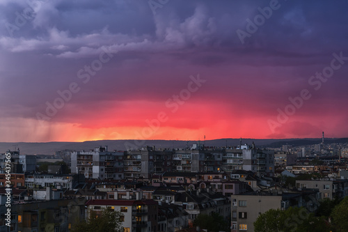 A storm is approaching the city in the late evening. Gleams of distant lightning reddened the sky above the hills outside the city. Scenic cityscape just before the storm. © Maryia