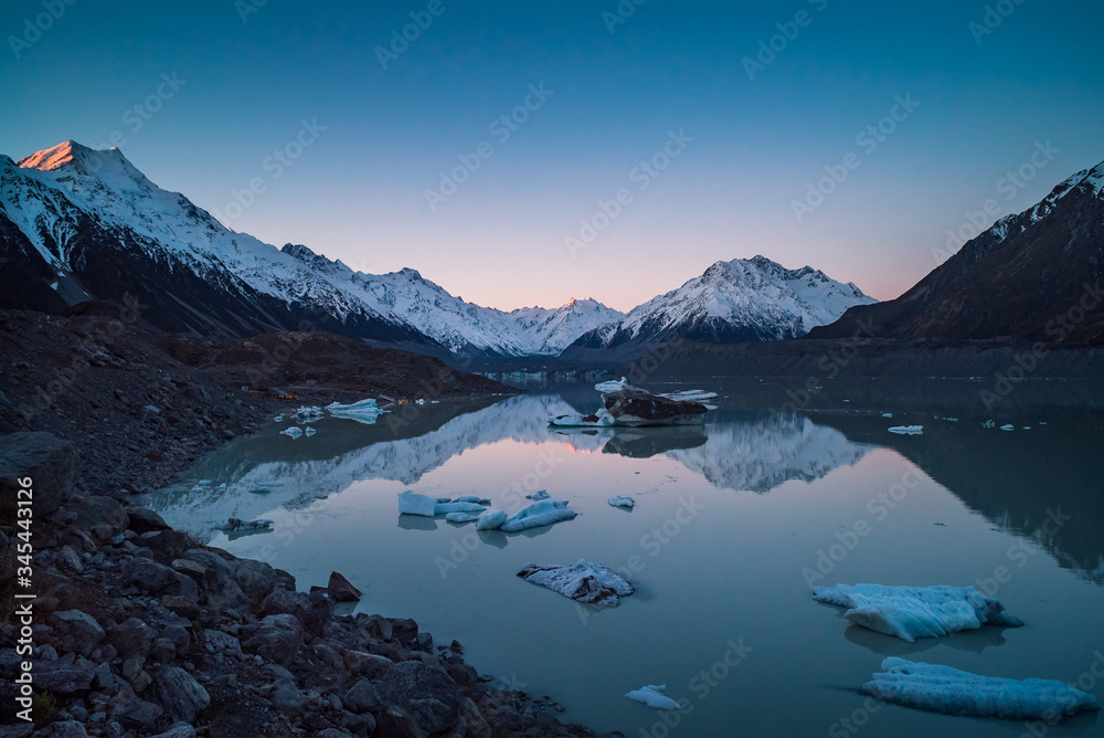 Late afternoon reflections of mountain peaks in turquoise melted glacier water filled with icebergs at Tasman Glacier river at Mount Cook, New Zealand