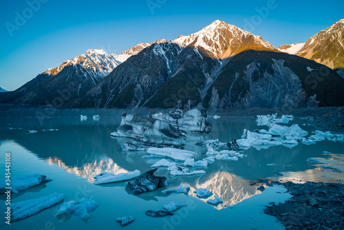 Late afternoon reflections of mountain peaks in turquoise melted glacier water filled with icebergs at Tasman Glacier river at Mount Cook, New Zealand