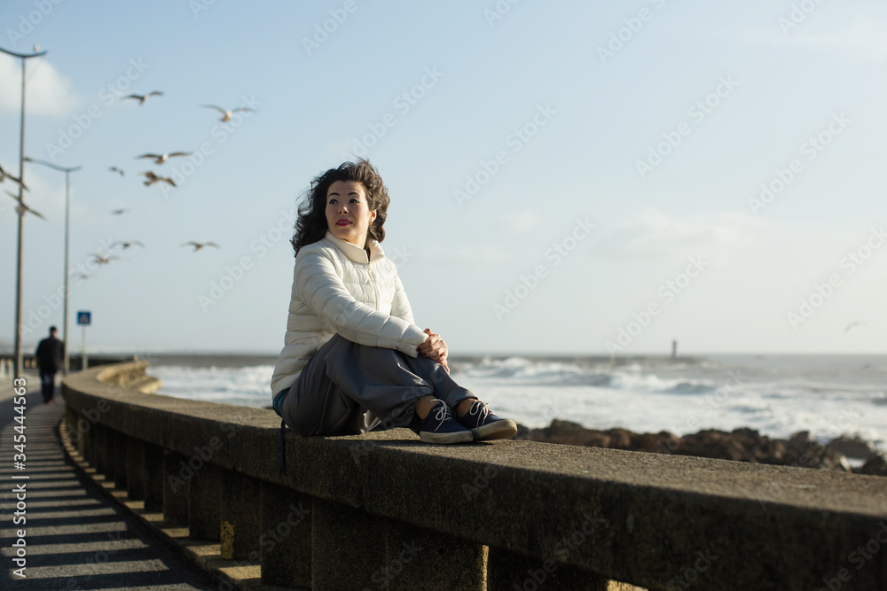 Multicultural woman sits on the waterfront during the surf and gulls around. Porto, Portugal.