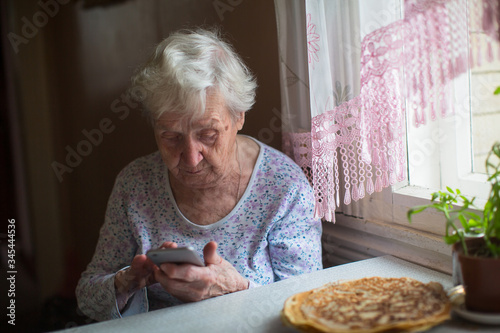 Elderly woman sits with a smartphone in her hands at home.