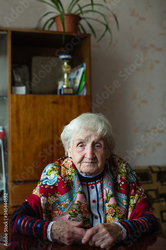 Old woman in bright clothes sitting at the table in her home.
