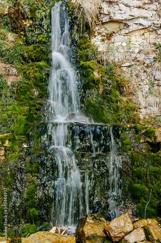Beautiful mountain waterfall among the stones. A source of water in arid areas. Motion blur, vertical photo