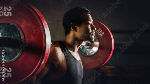 asian strong athletic man having workout and bodybuilding with barbells weight lifting backsquat style in gym and fitness center in dark tone photo