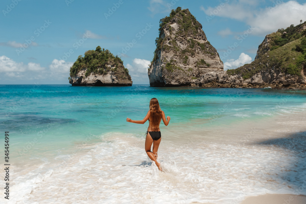 Woman running in water in beautiful lagoon on Nusa Penida island. Young, sporty, beautiful and fit woman walking on a summer beach, back view