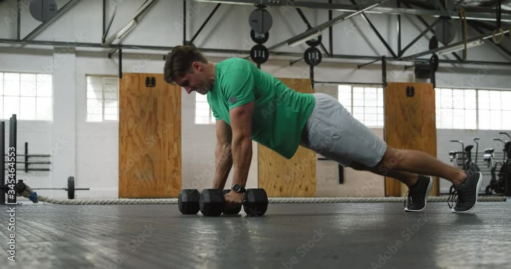 Side view athletic Caucasian man lifting alternate weights Side view athletic Caucasian man lifting alternate weights