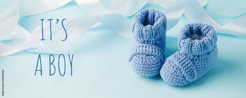 It's a boy text. Blue Baby knitted shoes for newborns on blue background, Minimal baby shower, newborn party background, copy space