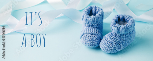 It's a boy text. Blue Baby knitted shoes for newborns on blue background, Minimal baby shower, newborn party background, copy space