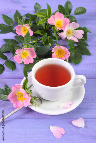 Cup of tea and wild rose flower on purple boards