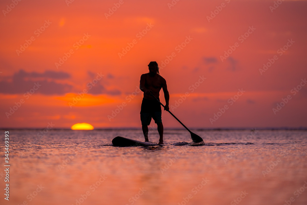 surfer rides by paddle board (S.U.P.) in the ocean against the background of a large disk of the setting sun