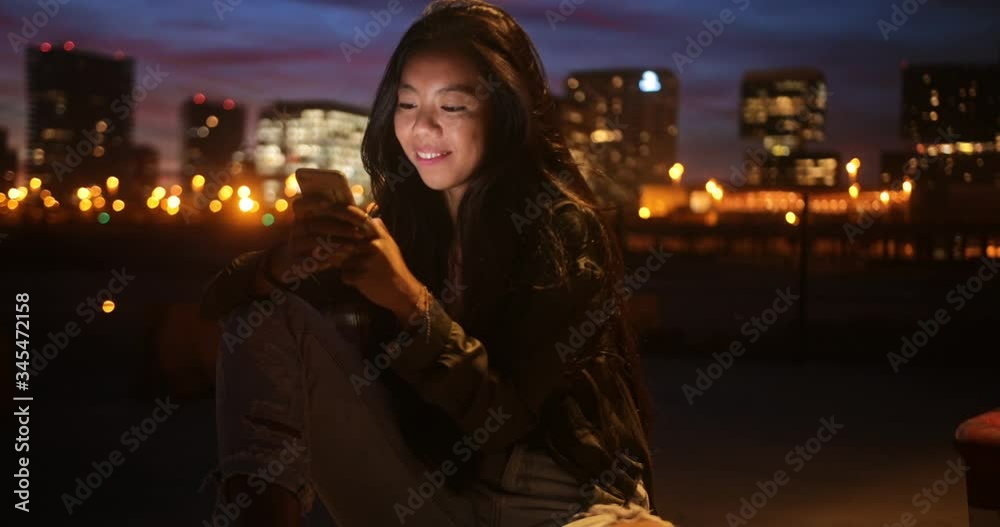 Happy hipster Asian woman text messaging in city at night Happy hipster Asian woman text messaging in city at night