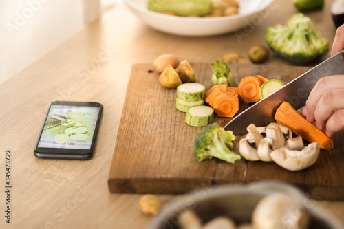 Cooking online or learning cooking concept. Man preparing vegan dish steamed vegetables while watching recipe on the Internet using smartphone photo